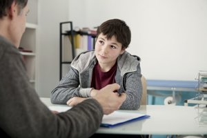 A preteen boy sits at a table while he listens to a child psychiatrist houston trusts