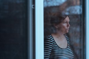 A woman somberly looks out a window as she ponders if she may need a Houston seasonal affective disorder therapy psychiatrist